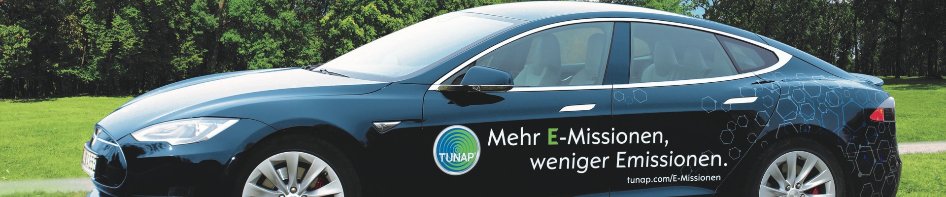 Side view of a dark blue sports car with white lettering and a TUNAP logo on a green meadow