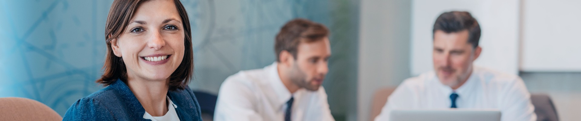 Portrait of a smiling young businesswoman sitting at a table with colleagues working in the background